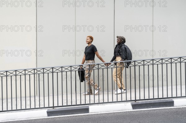 Two people walk hand in hand, smiling outdoors, expressing love and unity as a multiethnic couple. Casual attire, urban setting, showcasing an uplifting scene of connection