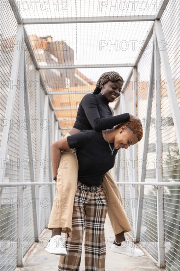 Two people share a joyful moment on a pedestrian bridge, with one playfully giving the other a piggyback ride, capturing the essence of love and happiness