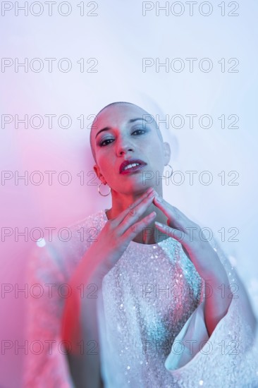 Middle-aged woman with shaved head in stylish pose, adorned with intricate attire. Artistic lighting creates a dreamy ambiance, highlighting her confident expression