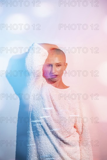 Middle-aged woman with shaved head poses confidently in creative lighting. The colorful bokeh effect adds a dynamic, artistic touch to the minimalist portrait