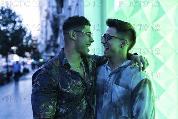 Latin gay couple enjoying an evening in the city, sharing laughter and embracing under vibrant neon lights. Their happiness is contagious, reflecting genuine connection and fun