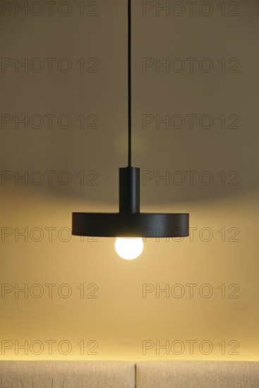 A modern hotel room showcases a sleek pendant light against a warm, neutral wall. The glowing bulb casts a cozy ambiance, enhancing the room's contemporary design