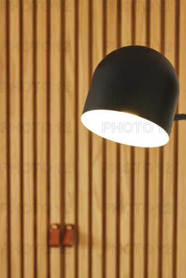 A modern hotel room featuring a sleek black lamp illuminating wooden panel walls. The warm lighting complements the elegant and cozy ambiance of the space