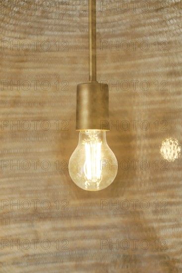 A warm, glowing light bulb hangs within a rustic hotel room, casting a cozy ambiance. The elegant design complements the chic decor, creating a welcoming atmosphere