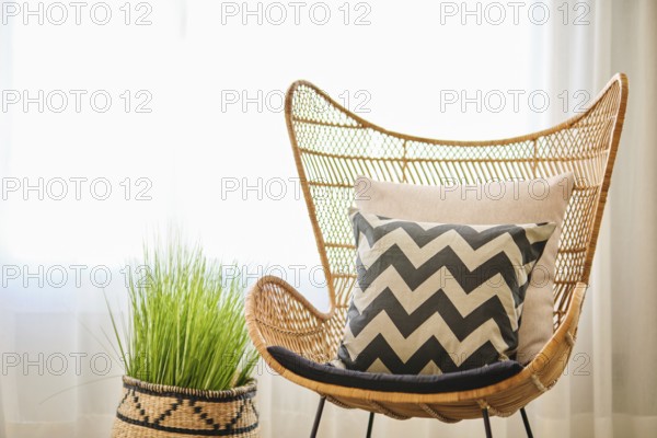 A beautifully decorated hotel room featuring a wicker chair, chevron-patterned cushion, and a woven basket with greenery. Natural light complements the warm, earthy tones