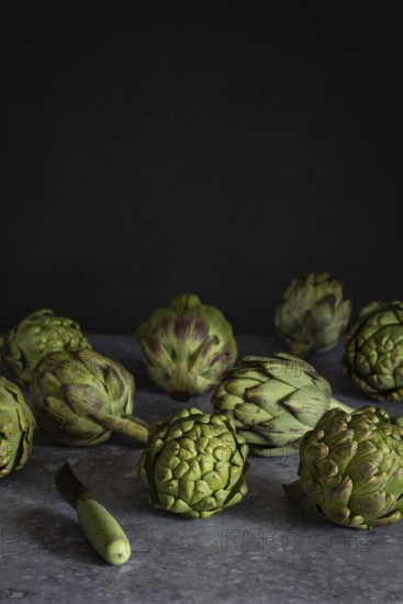 Fresh artichokes arranged artfully on a dark, textured surface, ideal for culinary and healthy living concepts. The contrast highlights their rich green tones