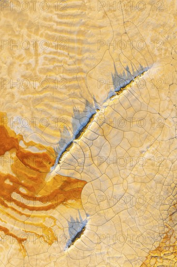 Aerial view of cracked mud in vibrant hues, showcasing an abstract pattern of orange, blue, and beige The intricate design highlights the beauty of natural textures