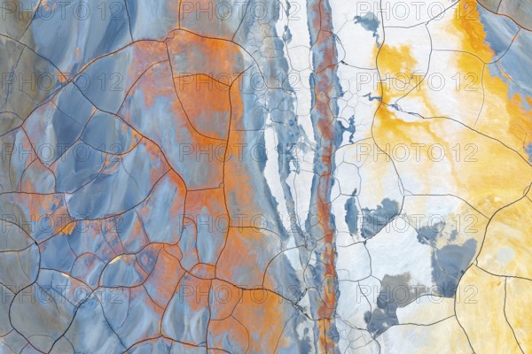 Aerial view of multicolored cracked mud showing vibrant hues of blue, orange, and yellow This abstract natural pattern resembles a dynamic, artistic painting