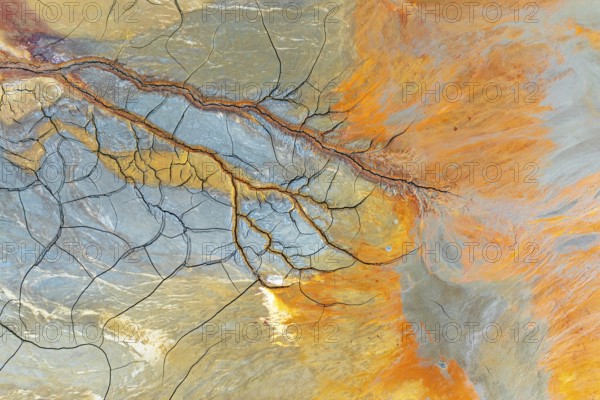 Aerial perspective of vibrant multicolor mud patterns and textures The image showcases natural, flowing designs in earthy tones of orange, blue, and brown, intersected by fine lines