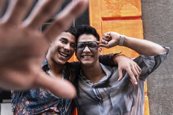 A smiling couple poses playfully in front of a bright orange wall. One partner playfully reaches out towards the camera, capturing their joyful connection