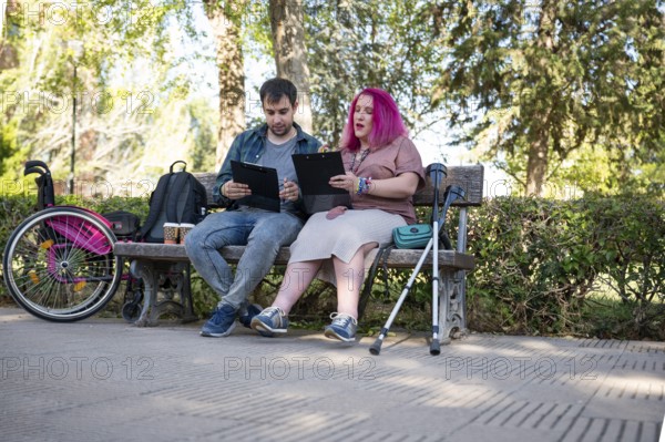 A college couple sits on a bench, studying with clipboards The woman, managing a disability due to spina bifida, uses a wheelchair and crutches, highlighting inclusivity