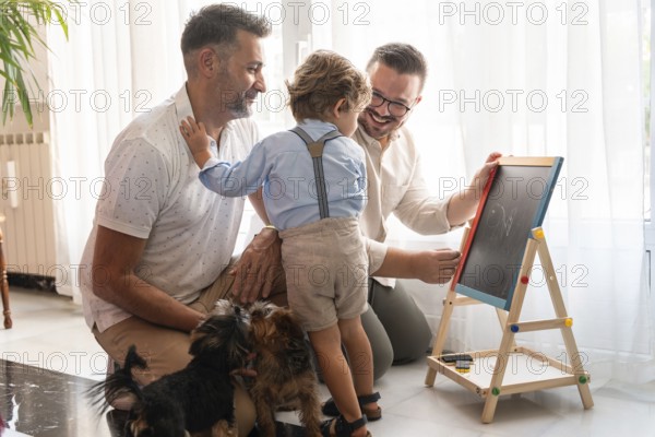 A joyful moment with a gay couple and their son drawing on a chalkboard, surrounded by playful dogs. Family love and creativity shine in a bright, cozy room