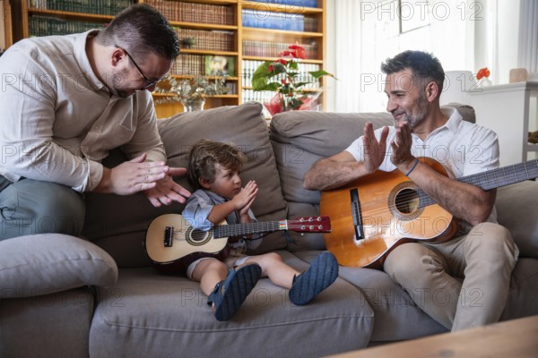 A loving gay couple enjoys quality time with their young son, playing guitars in the cozy living room. They share smiles and applause, fostering creativity and connection