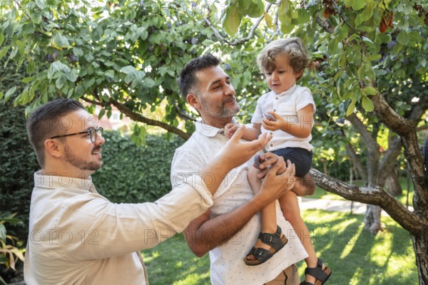 A joyful scene of a gay couple spending quality time with their young son outdoors. They are in a lush garden, symbolizing love, family bonding, and inclusivity