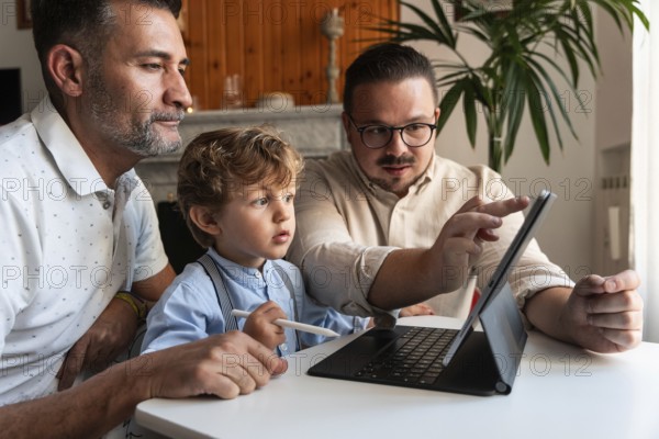 A loving gay couple enjoys quality time with their young son while using a tablet. The family is engaged in learning and playing in a cozy home environment