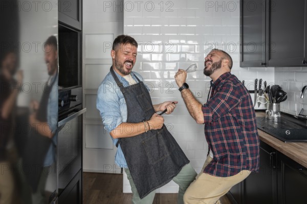 A cheerful gay couple enjoys a playful moment in their modern kitchen, passionately dancing and singing with kitchen utensils. They are sharing laughter and happiness