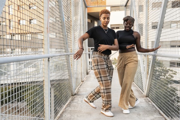 A joyful LGBT multiethnic couple dances on a city bridge, sharing a moment of connection and happiness. The casual atmosphere highlights their playful bond in an urban setting
