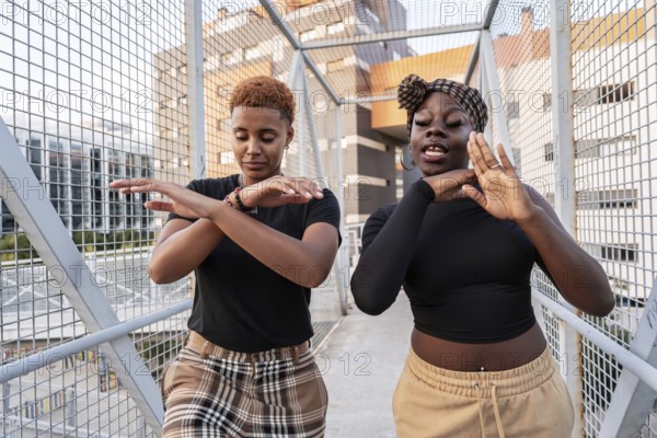 A lively LGBT multiethnic couple dances energetically on an urban bridge, expressing joy and freedom. The cityscape in the background captures their spirit and connection