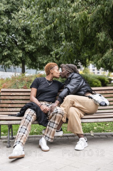 A loving LGBT multiethnic couple shares a tender kiss while sitting on a bench in a lush park. The multiethnic couple is dressed casually, enjoying a peaceful moment surrounded by greenery