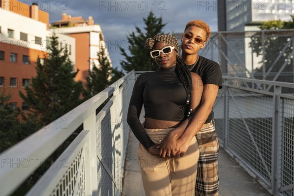 A loving LGBT multiethnic couple embraces warmly on a sunny urban bridge. They share a joyful and intimate moment amid the cityscape, showcasing their connection and love