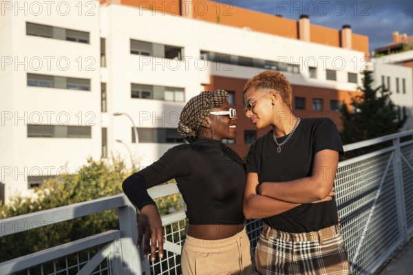 A loving LGBT multiethnic couple shares a tender moment on a sunny day, standing by a rail with modern buildings in the background, reflecting joy and connection