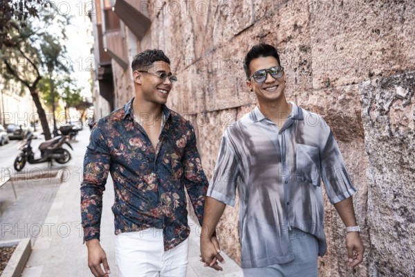 A joyful latin gay couple walks hand in hand down a lively street in Madrid. They're smiling, wearing stylish outfits and sunglasses, enjoying the sunny day and vibrant city atmosphere