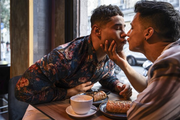 A loving latin gay couple shares a tender moment at a cafe, enjoying breakfast together. The intimate scene captures their affection and connection over coffee and pastries