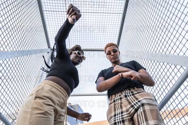 A lively LGBT multiethnic couple enjoys their day against an urban backdrop. They wear stylish outfits, exuding energy and expression, highlighting diversity and love in an urban environment