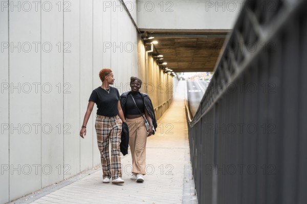 A joyful LGBT multiethnic couple walks side by side through a well-lit urban underpass, sharing a moment of happiness and connection in a modern cityscape