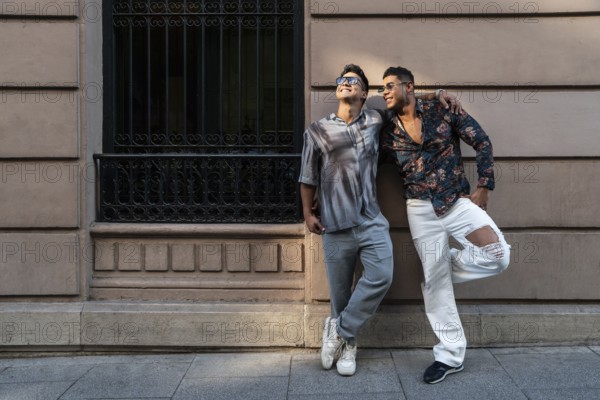A latin gay couple enjoys the sunny weather in Madrid, exuding happiness and authenticity. Captured in a lively urban setting, their casual outfits and bright smiles reflect joy and love