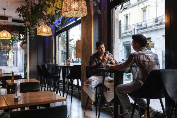 A latin gay couple enjoying a moment in a stylish café, surrounded by chic interior and warm lighting, highlighting a cozy yet modern urban setting