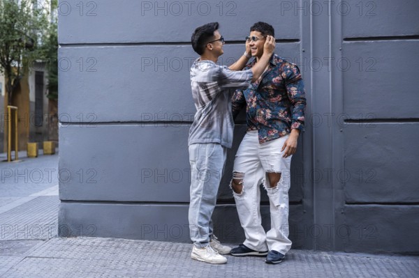 A latin gay couple enjoys a playful moment on an urban street, showing affection. They wear casual clothing with distinctive patterns and textures, embodying modern style