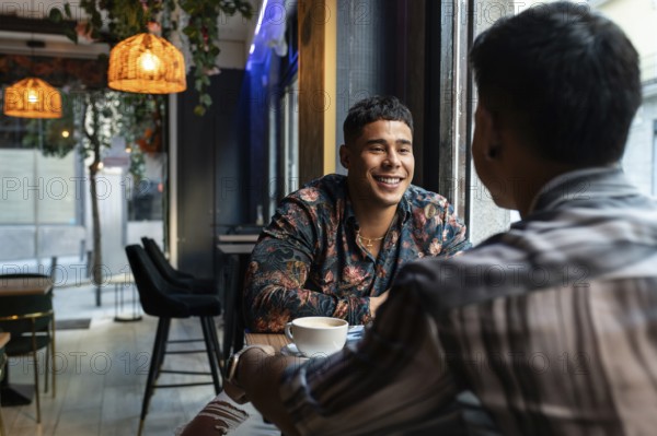 A latin gay couple shares smiles and conversation in a stylish cafe. Warm lighting and contemporary decor create a welcoming ambiance for their coffee date