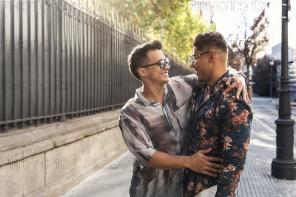 A joyful latin gay couple shares a warm embrace and smiles while walking on a sunny day in the vibrant streets of Madrid, illustrating love and companionship