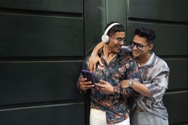 A joyful latin gay couple embraces while listening to music. One wears headphones and a floral shirt, the other sports a watch and sunglasses, expressing love and happiness
