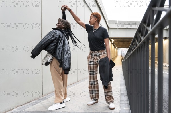 A happy LGBT multiethnic couple dances in an urban passageway, enjoying a playful moment together. The scene captures movement, happiness, and a sense of connection