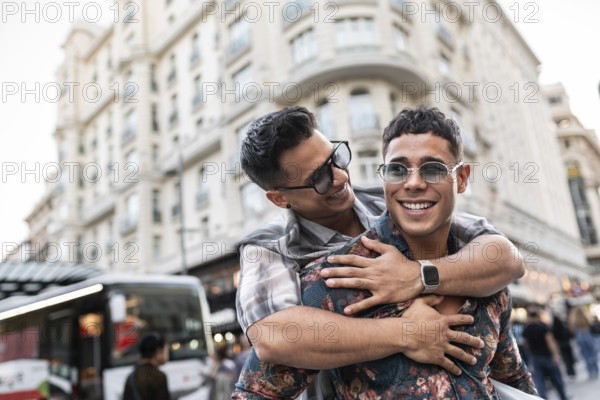 A joyful latin gay couple shares a playful embrace on a lively street in Madrid. The energy of the bustling city and their happiness capture the essence of love and urban life