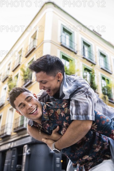 A joyful latin gay couple share a playful piggyback ride in the vibrant streets of Madrid. The warm atmosphere captures their happiness and connection, set against a charming urban backdrop