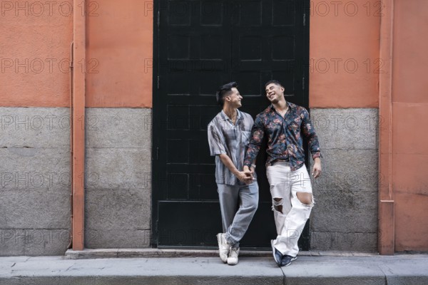 A joyful latin gay couple shares a tender moment holding hands, standing in front of a colorful urban backdrop in Madrid, Spain, capturing the essence of love and happiness
