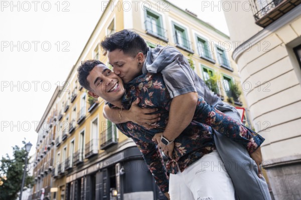 A joyful latin gay couple enjoys a playful moment on the streets of Madrid. They show affection with laughter and a warm embrace, capturing the vibrant energy of the city