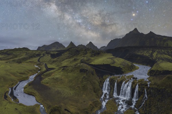 Captivating Icelandic scene with a lush green landscape, a winding river, and a cascading waterfall, set beneath a mesmerizing star-filled night sky