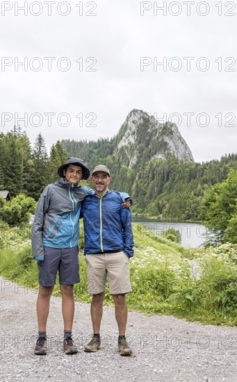 A father and son enjoy a hiking adventure at Lac de Taney, Switzerland, surrounded by lush greenery and a majestic mountain backdrop The scene captures the joy of nature exploration