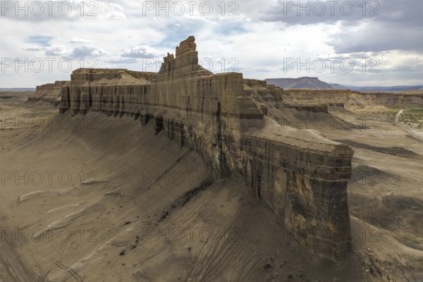 A dramatic aerial view of Caineville Mesa, Utah, showcasing towering rock formations and expansive desert landscape under a partly cloudy sky A testament to nature's grandeur