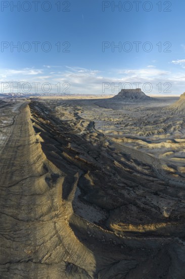 Aerial view of Caineville Mesa in Utah, showcasing rugged terrain and dramatic shadows under a vast blue sky The desert landscape highlights geological formations