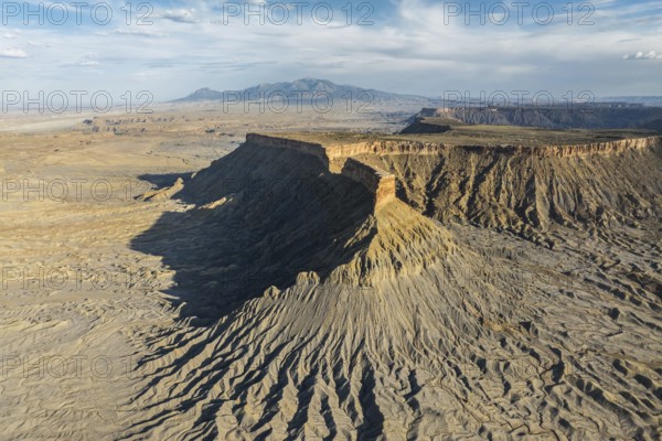 Dramatic aerial view of Caineville Mesa in Utah, USA, showcasing rugged terrain, layered rock formations, and expansive desert vistas under a vast sky