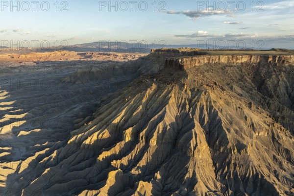 Aerial view of Caineville Mesa, Utah, showcasing dramatic ridges and rocky terrain under a clear sky The golden light accentuates the unique formations of this desert region