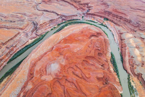 Stunning aerial shot capturing the sinuous Rio San Juan winding through the dramatic red rock formations in Utah, USA. The vibrant orange and red hues contrast vividly with the lush green riverbanks