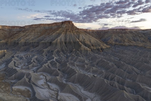 Captivating vista of Caineville Mesa in Utah, USA, showcasing dramatic rugged terrain and striking geological formations under a colorful sunset sky, ideal for nature enthusiasts