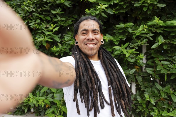 A cheerful man with long dreadlocks smiles while taking a selfie in a lush green garden in Barranco, Lima, Peru The vibrant foliage adds to the lively atmosphere