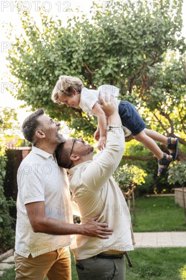 A joyful gay couple playing with their young son in a sunlit garden, capturing a heartwarming, affectionate family moment filled with love, laughter, and connection